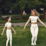 Mother and daughter bonding through outdoor exercise in activewear, featuring a joyful moment in a green park.